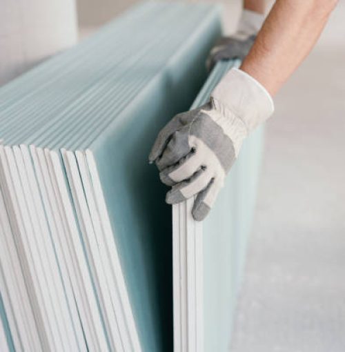 Builder taking a sheet of chip board cladding from a stack against the wall with his gloved hands indoors in a new build home